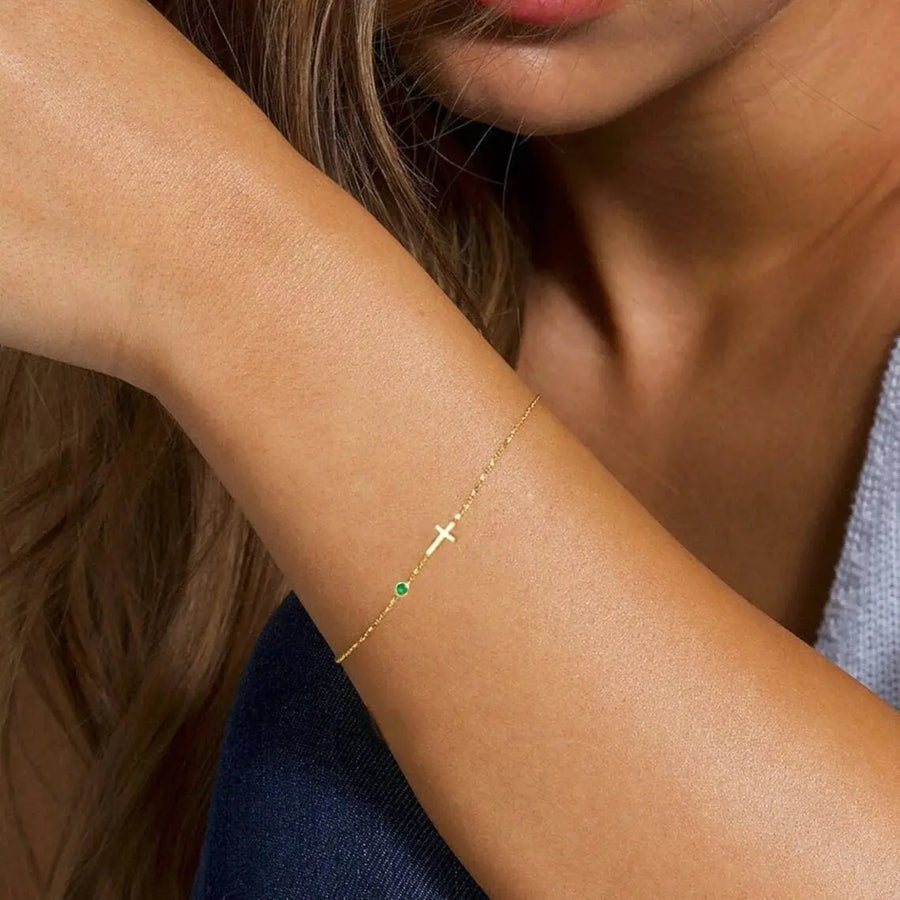 Gold-filled cross birthstone bracelet arranged as a birthday gift on an ivory surface