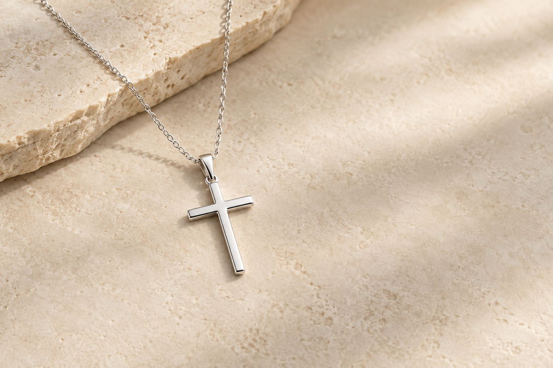 Simple silver cross necklace on a warm neutral stone background