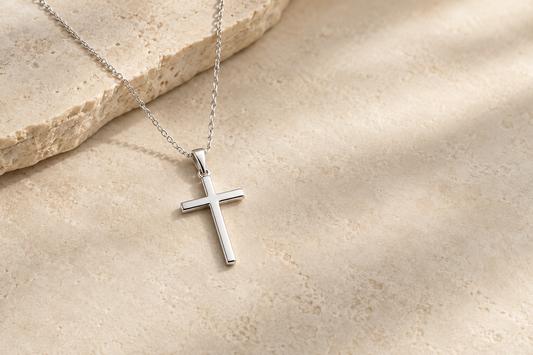 Simple silver cross necklace on a warm neutral stone background